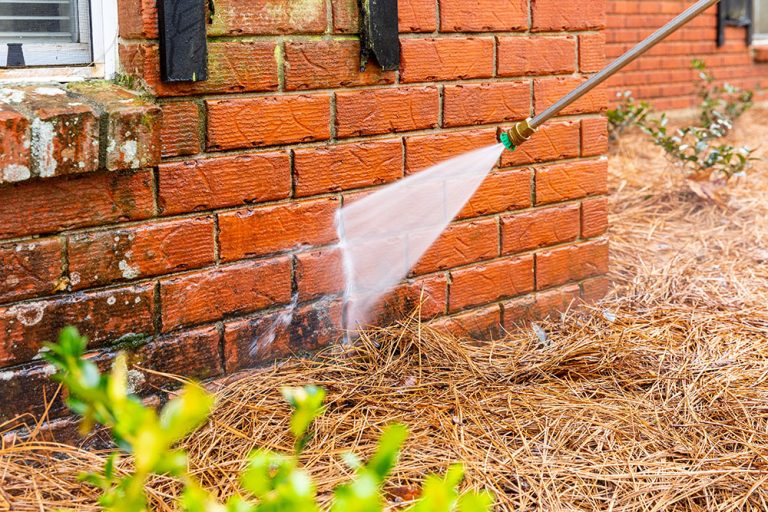 Dirty brick wall being cleaned with a pressure washer.