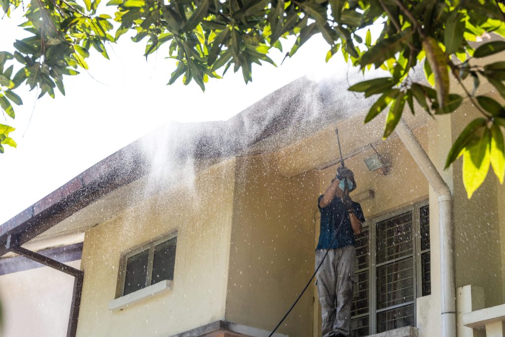 Worker using high pressure water jet spray gun to wash and clean dirt from roof ceiling